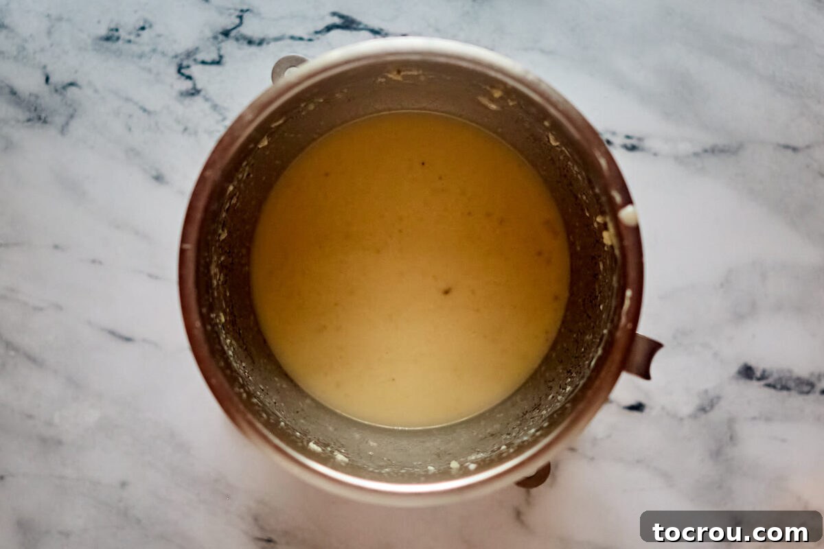 Mashed potatoes mixed with butter, egg, and warm milk mixture in mixer bowl.