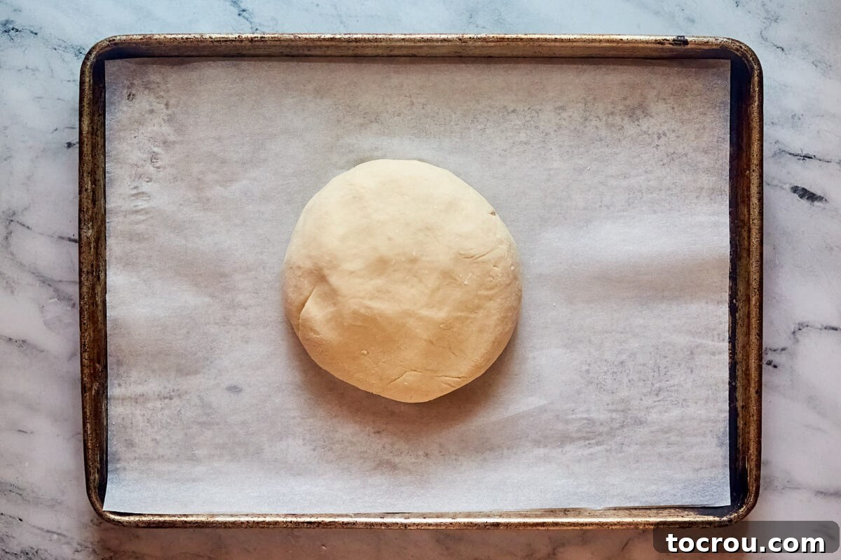 Ball of potato bread dough on parchment lined baking sheet.