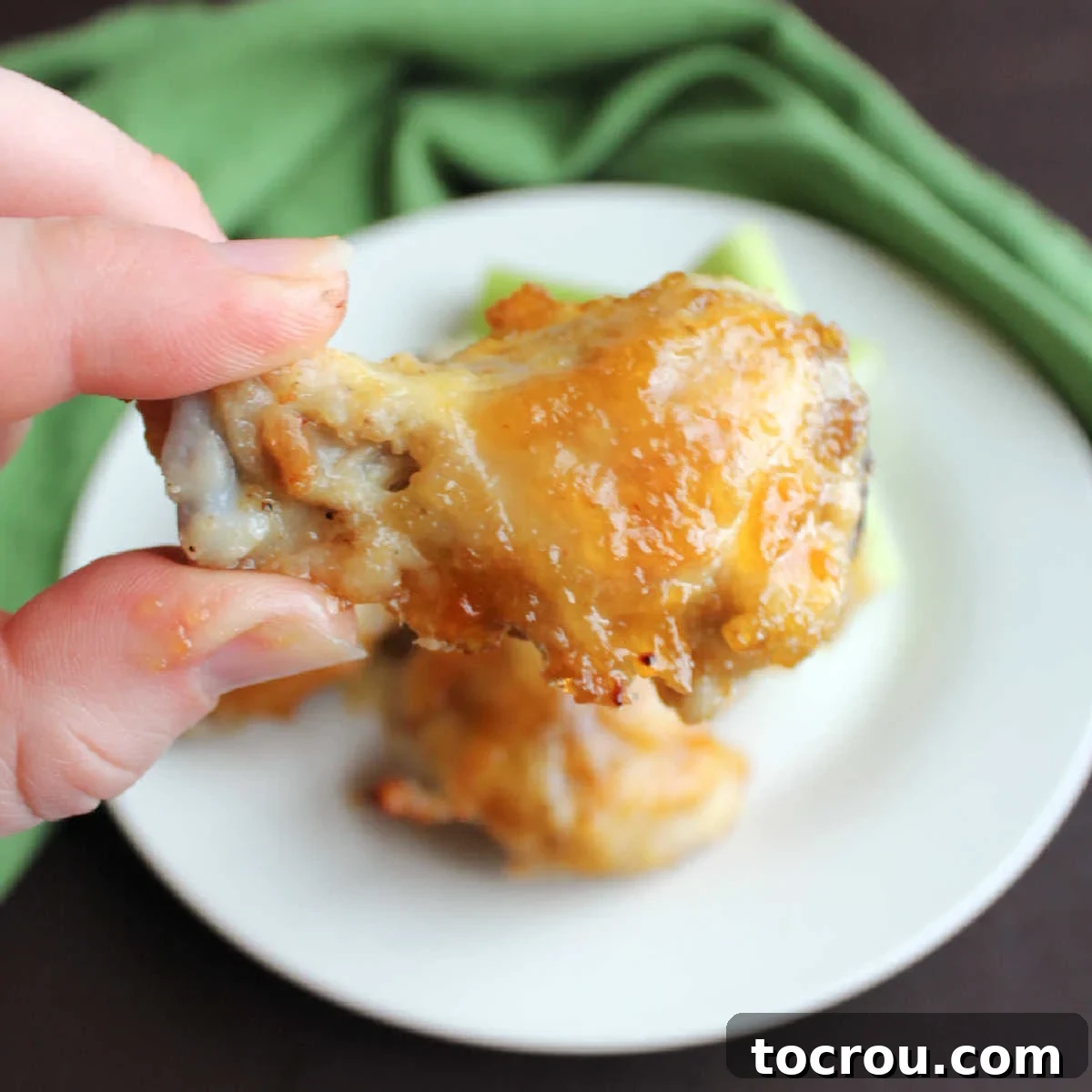 A little sweet and a little heat will have you licking your fingers and coming back for more! Peach habanero chicken wings are perfect game day food. Hand holding a juicy, perfectly glazed peach habanero chicken wing drummie.