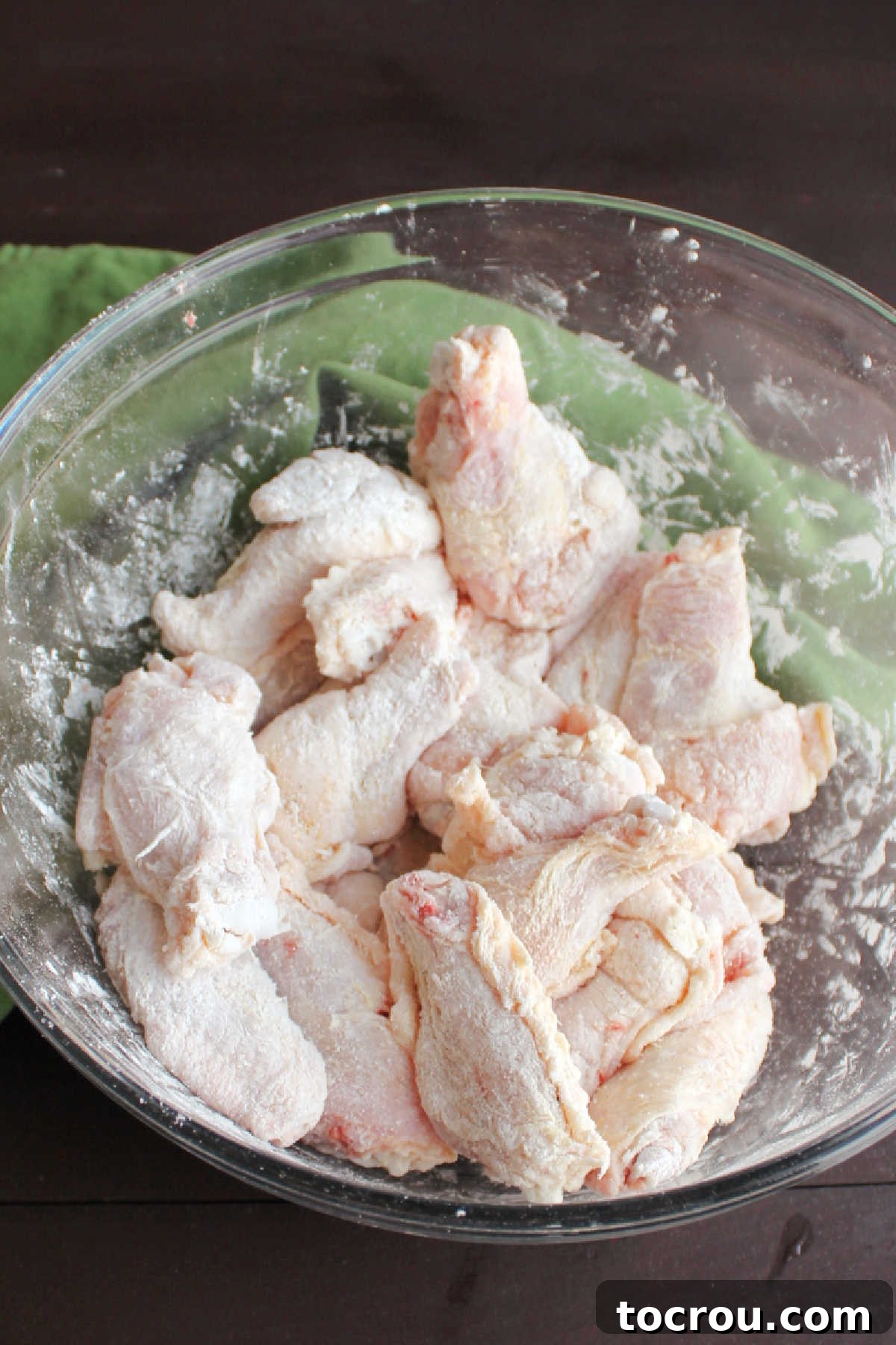 Wings getting coated in spices for maximum crispiness. Raw chicken wing pieces being coated with a dry spice rub, cornstarch, and baking powder in a large mixing bowl.