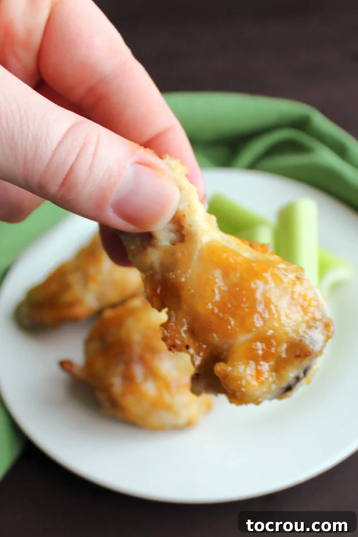 Enjoying a delicious peach habanero wing. Close-up of a hand holding a single, perfectly glazed baked peach habanero chicken wing, showcasing its sticky, appetizing coating.