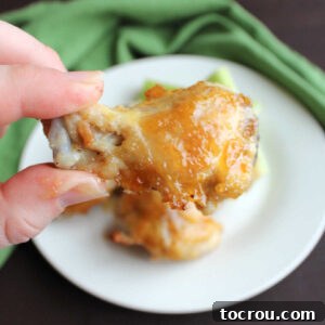 Hand holding wing drummie coated in peach habanero sauce.