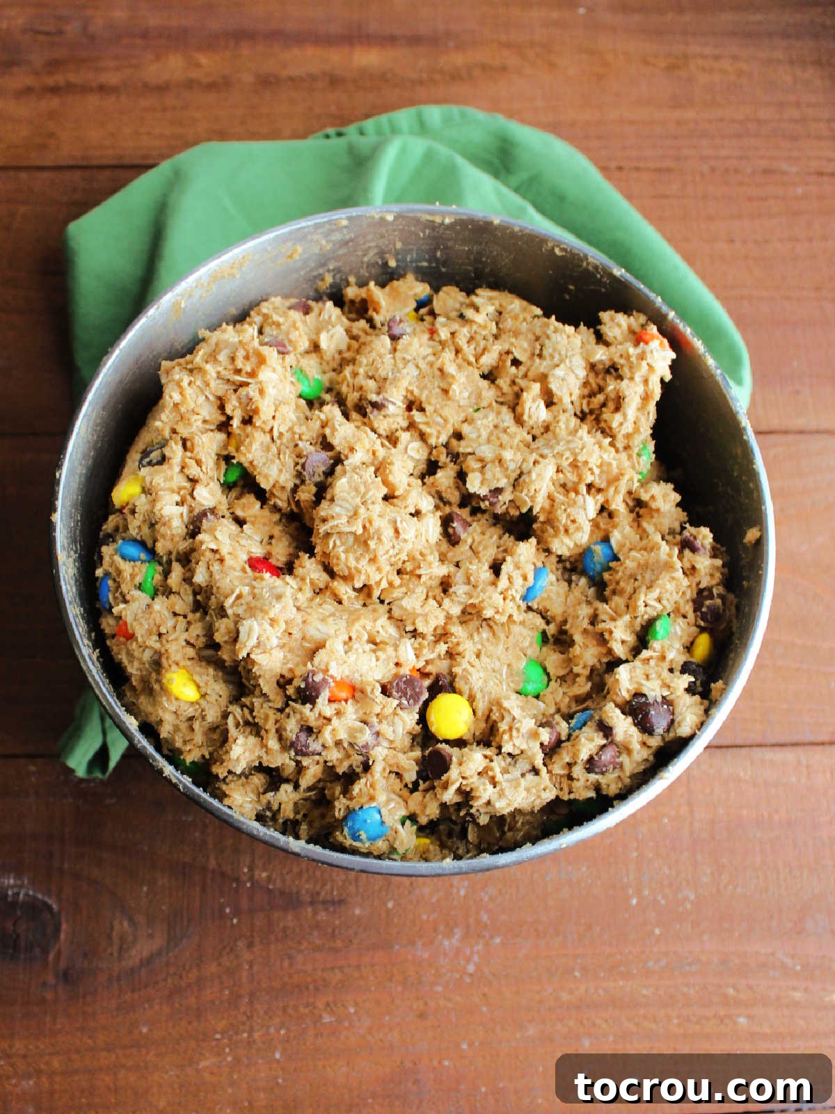 Monster Cookie Dough in the Mixer Mixer bowl filled to the brim with monster cookie dough featuring peanut butter, oatmeal, and chocolates.