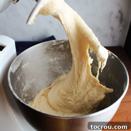 Lifting dough hook out of mixer bowl showing slack dough inside.