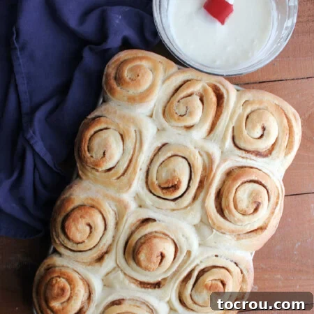 Freshly baked potato cinnamon rolls with golden brown tops next to a mixing bowl with vanilla icing inside.