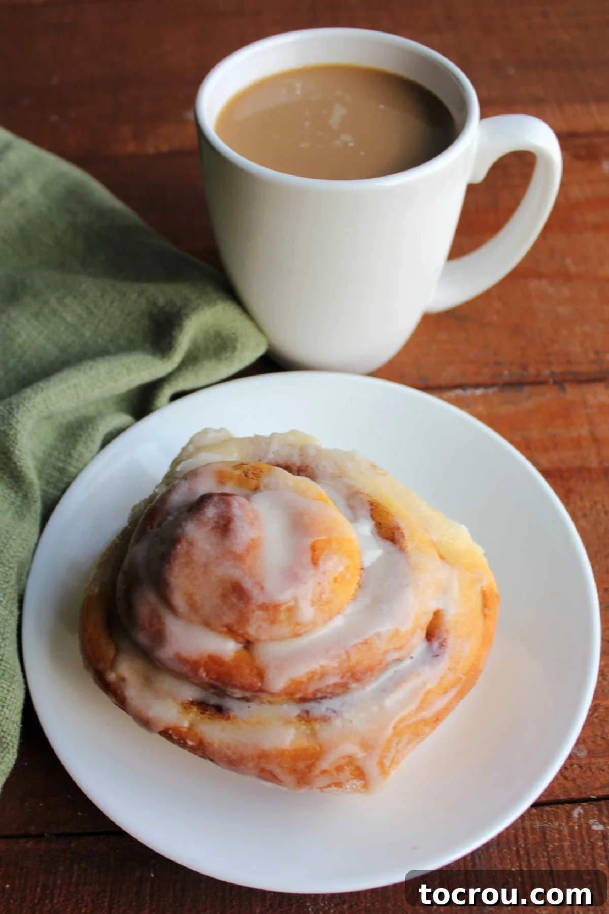 Plate with an iced mashed potato cinnamon roll with a mug of coffee.