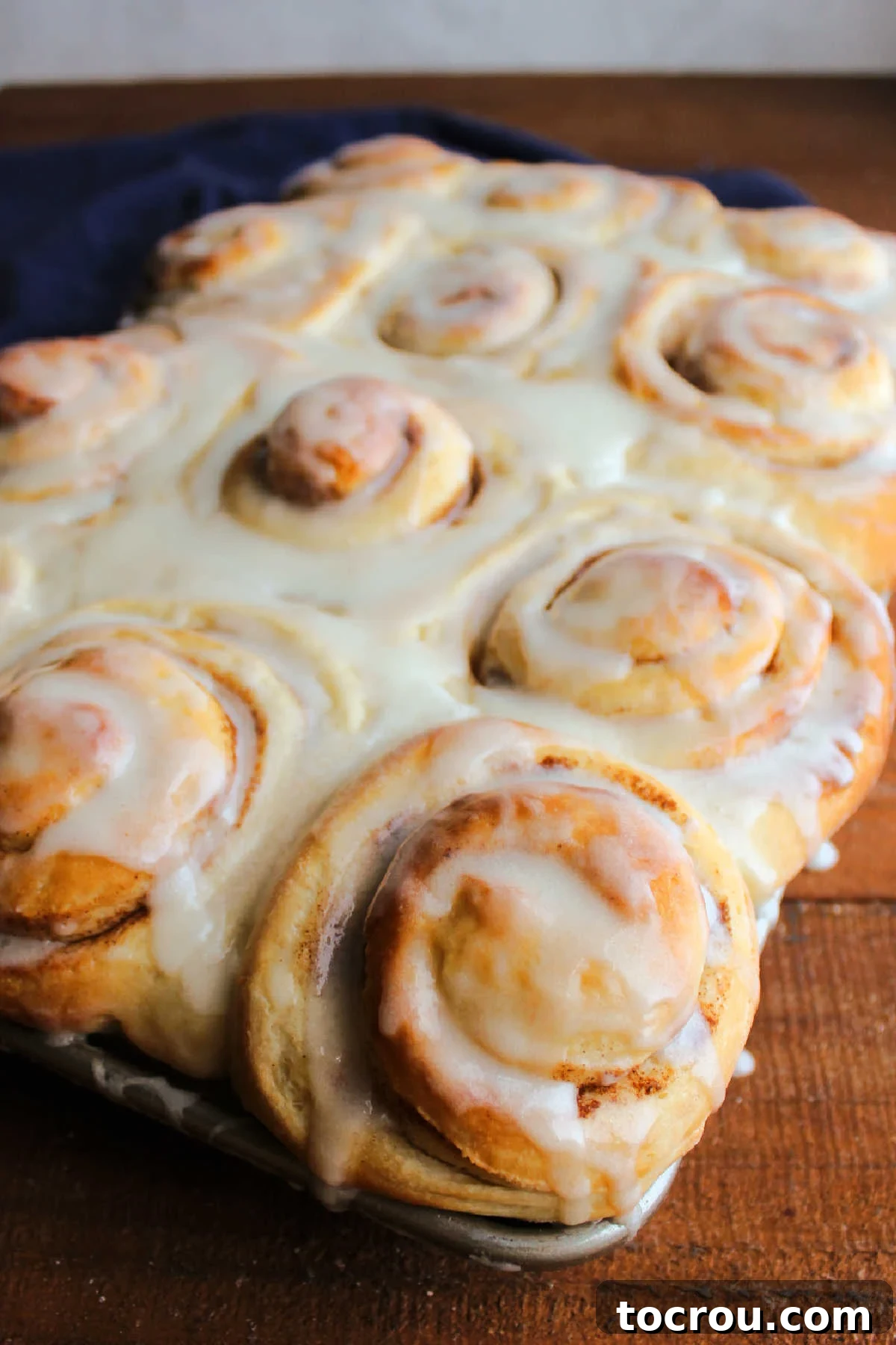 Tray of iced cinnamon buns with some of the icing dripping over the edge.
