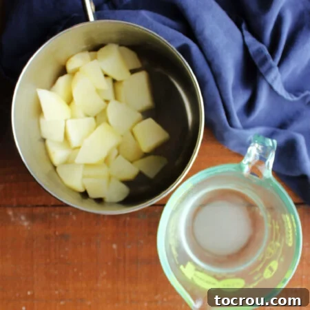 Saucepan with cooked chunks of potatoes in it next to a measuring cup with water from the cooked potatoes and sugar inside.