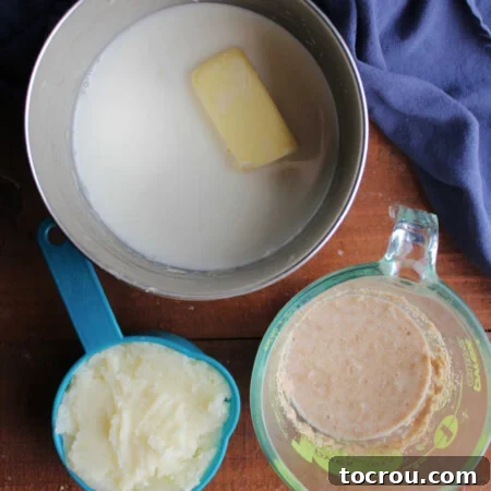 Milk, butter, and sugar in saucepan next to a cup of mashed potatoes and a measuring cup with yeast mixture in it.