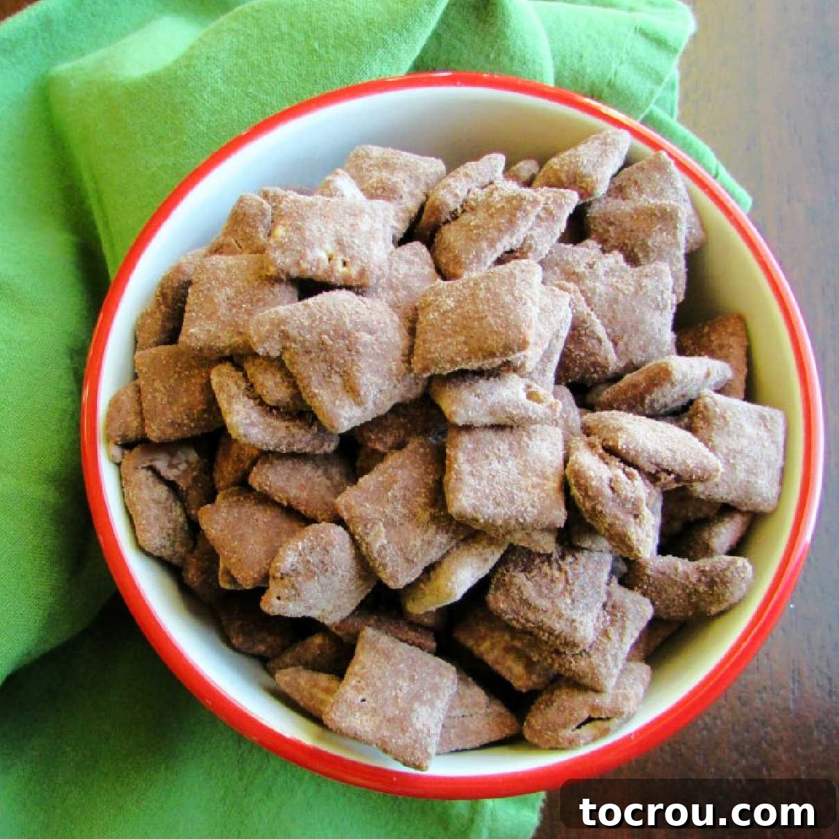 A close-up view of a bowl of rich brownie batter muddy buddies, ready for snacking. The crunchy cereal is coated in a dark, chocolatey peanut butter mixture, promising a decadent treat.