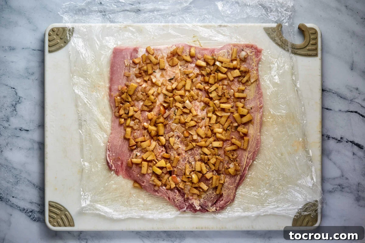 Apple Rosemary Filling Spread Out Cooked apple mixture spread over the top of the butterflied pork loin, ready to be rolled up.