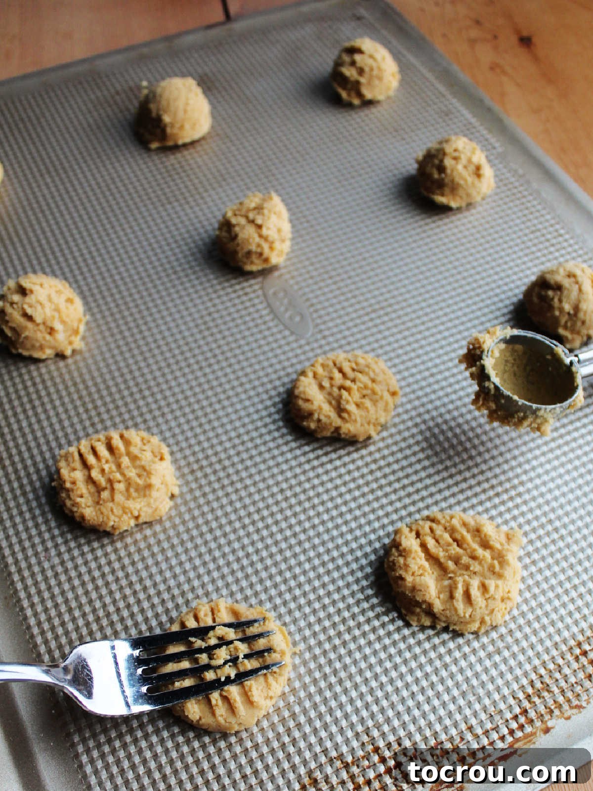 Grandma's Irresistible Peanut Butter Cookies 5 Tray of perfectly portioned peanut butter cookie dough balls, with a cookie scoop nearby and a fork pressing the classic crisscross marks into the top of a dough ball.