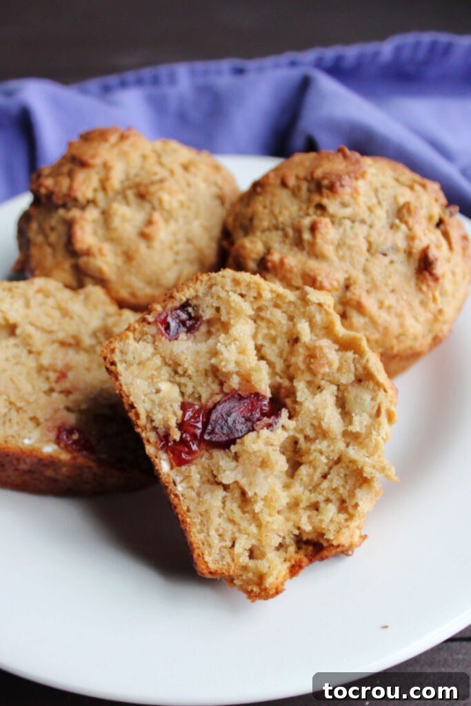 Plate of muffins showing the soft inside of one with visible cranberries and oats.