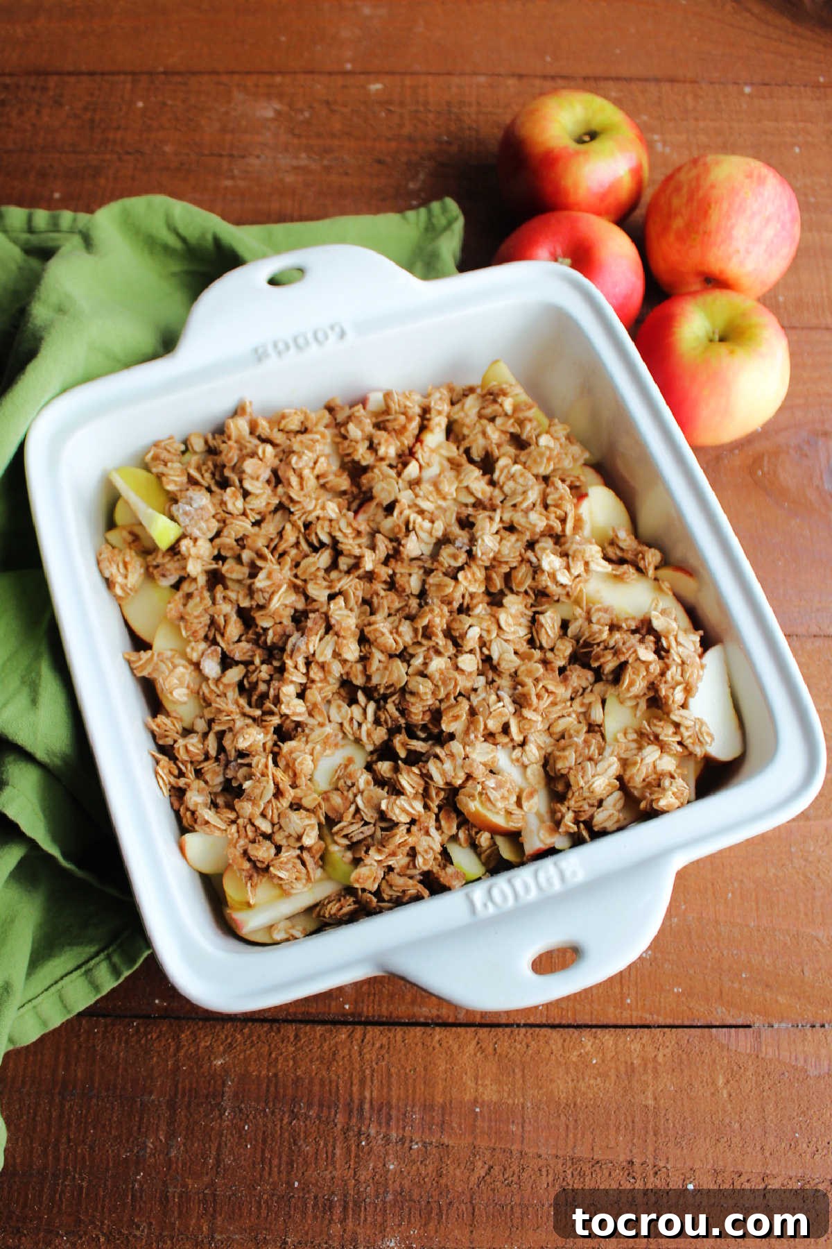 Square baking dish filled with fresh baked apple crisp, featuring golden, crumbly oat topping over tender apples.