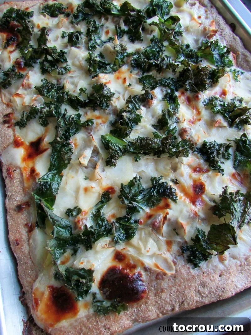 Zuppa Toscana Pizza with Detailed Toppings Close-up of a sheet pan pizza, highlighting the beautiful layers of creamy sauce, bubbling melted cheese, thinly sliced potatoes, savory Italian sausage, and vibrant green kale before being cut.