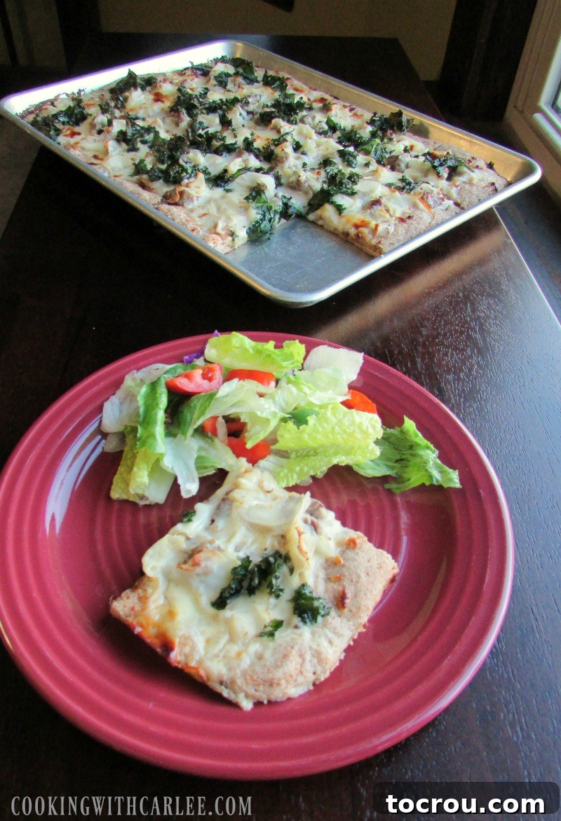 Zuppa Toscana Pizza Slice with Salad A single delicious slice of Zuppa Toscana pizza resting on a white plate, accompanied by a fresh green salad. In the background, the remaining sheet pan pizza awaits its turn.