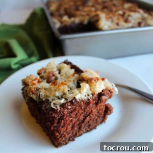Square piece of German chocolate cake topped with golden broiled coconut and pecan topping, glistening and ready to be enjoyed.