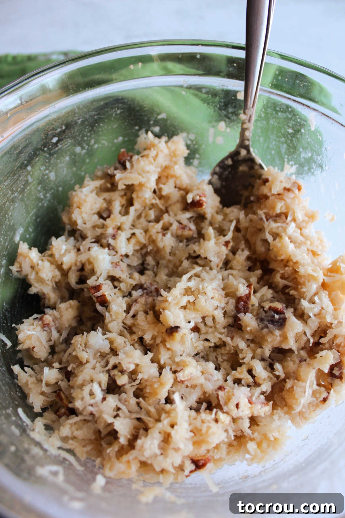 Decadent German Chocolate Cake Crowned with Broiled Coconut 8 A rich, brown coconut topping mixture, featuring brown sugar, pecans, butter, and milk, perfectly prepared in a bowl and ready to be spread onto the cake.