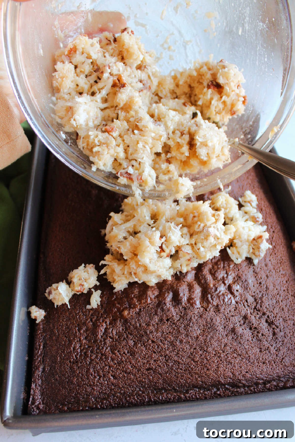Decadent German Chocolate Cake Crowned with Broiled Coconut 9 Hands carefully spreading the thick, textured coconut mixture evenly over a baked German chocolate cake, preparing it for its unique broiled finish.