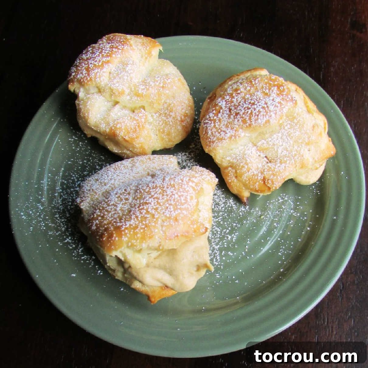 Three powdered sugar dusted cream puffs, generously filled with creamy pumpkin cream cheese mixture, presented on a rustic white plate.