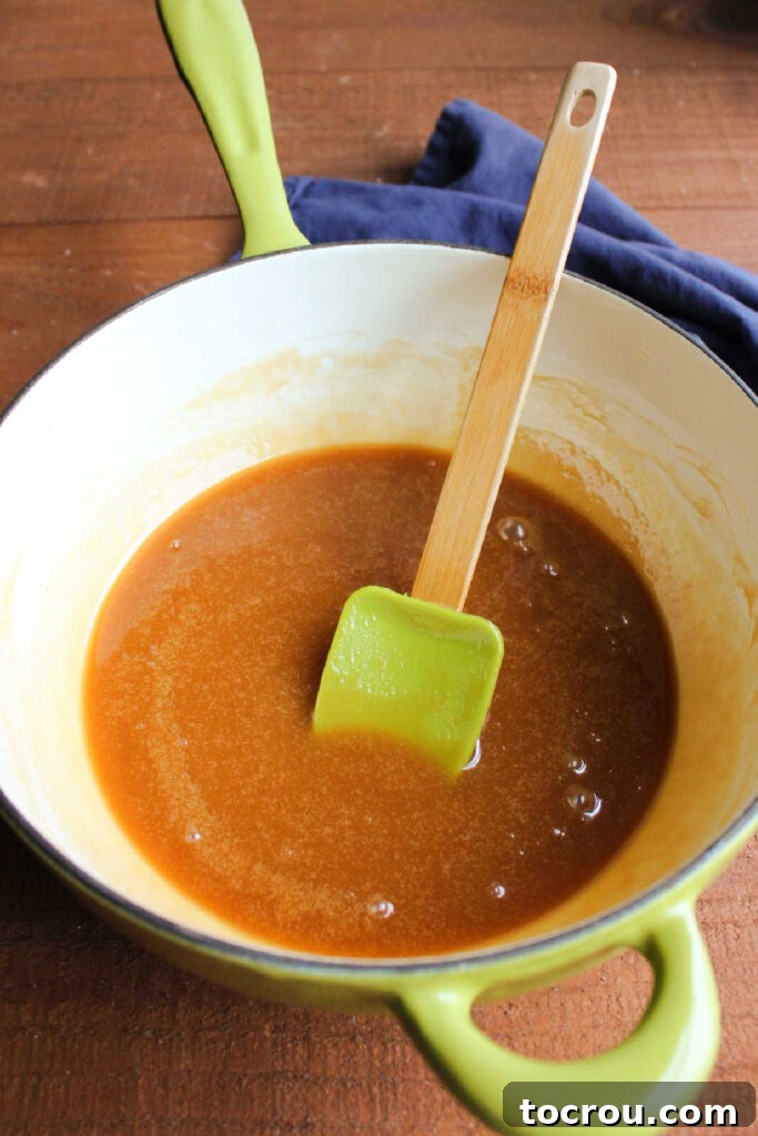 Enameled cast iron saucepan filled with freshly made apple cider caramel sauce and a spatula.