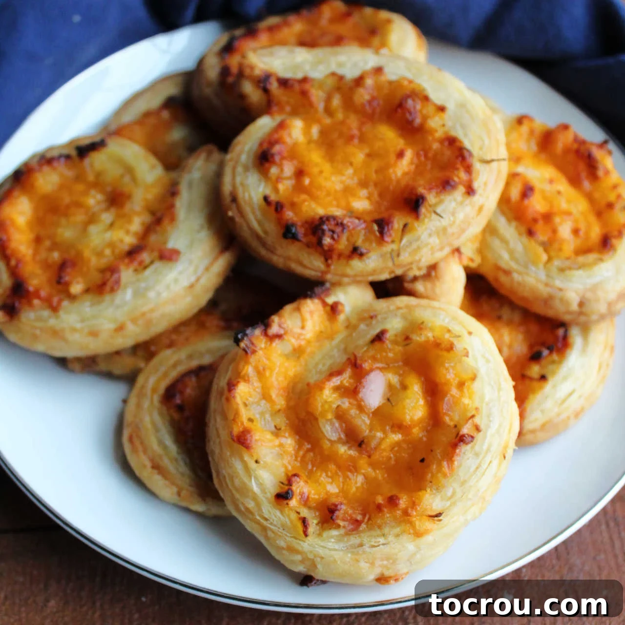 A plate brimming with golden brown puff pastry pinwheels, showcasing a savory filling of cheddar cheese, tender apples, and caramelized onion, ready to be enjoyed.