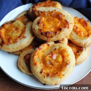 A delicious plate of golden brown puff pastry pinwheels with cheddar, apple and onion filling.