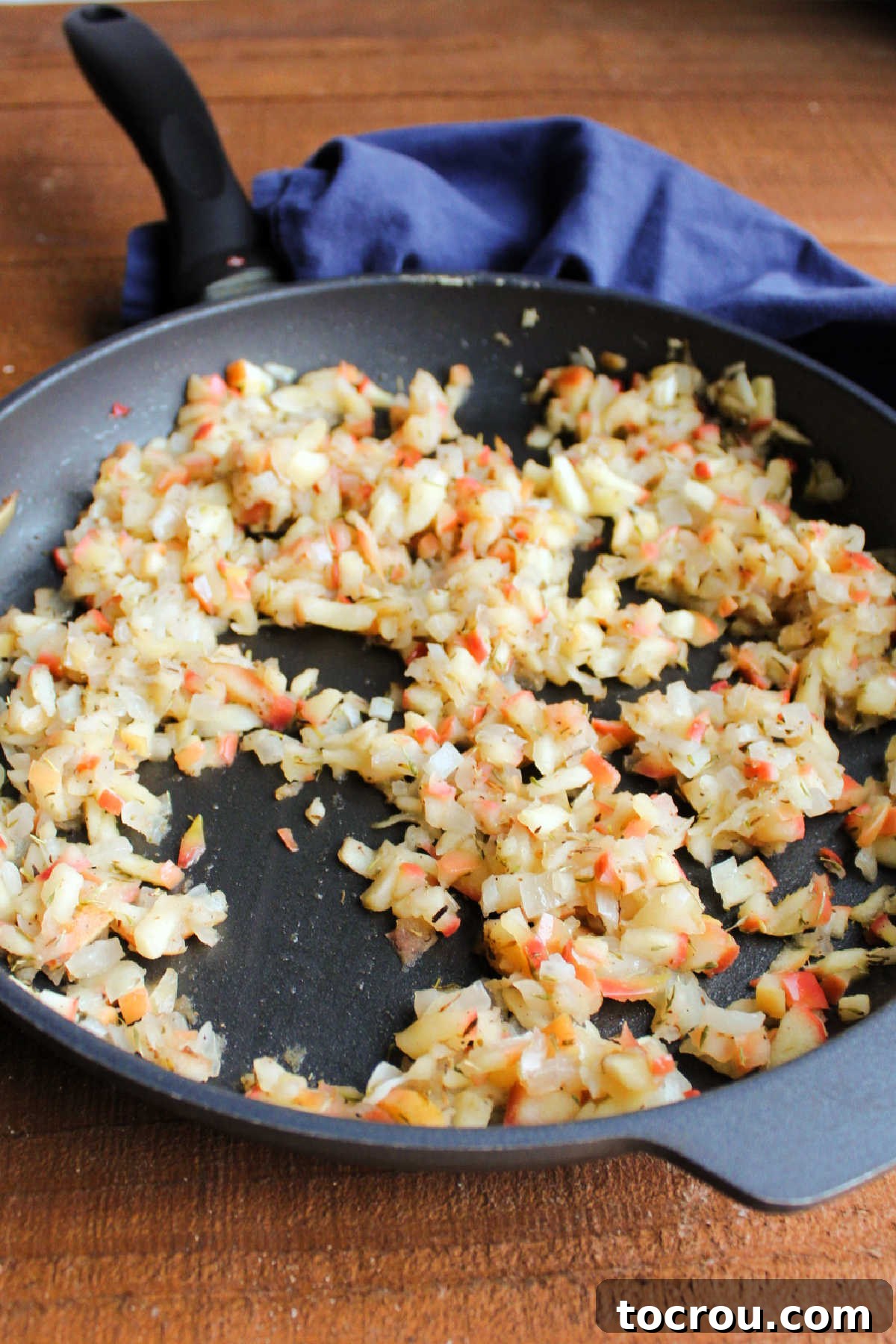 A cast-iron skillet filled with a cooked mixture of finely diced apples and translucent onions, steaming gently and ready to be cooled for the pinwheel filling.