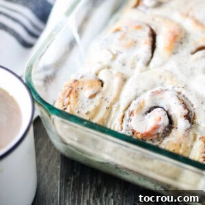 Corner of pan of coffee cinnamon rolls next to mug of coffee.