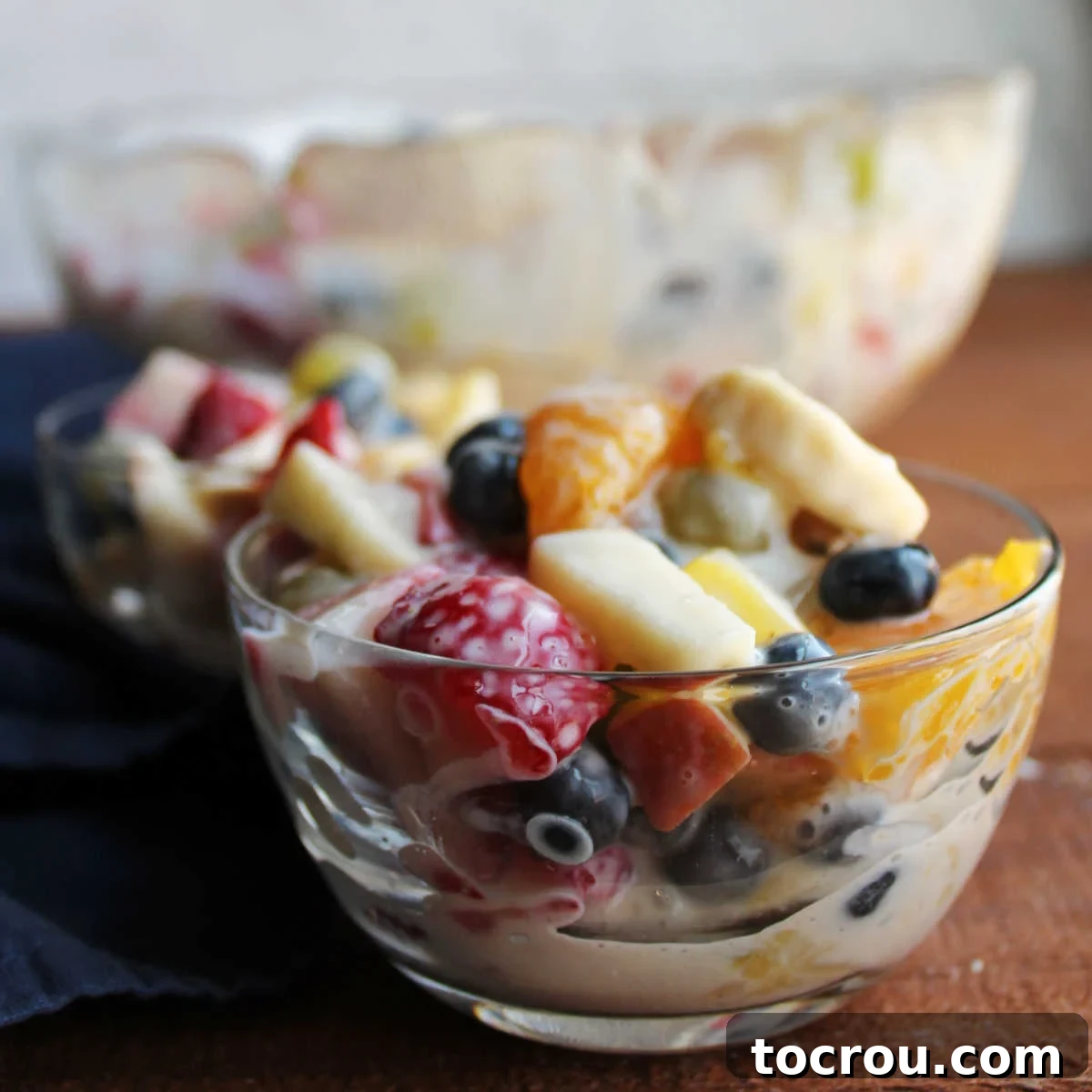 Small glass bowls of fruit salad with fresh berries, bananas, oranges, pineapple, and apples dressed with condensed milk and lemon juice.