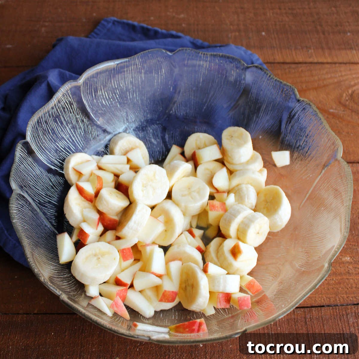 Chopped apple and banana slices tossed in lemon juice in glass salad bowl.