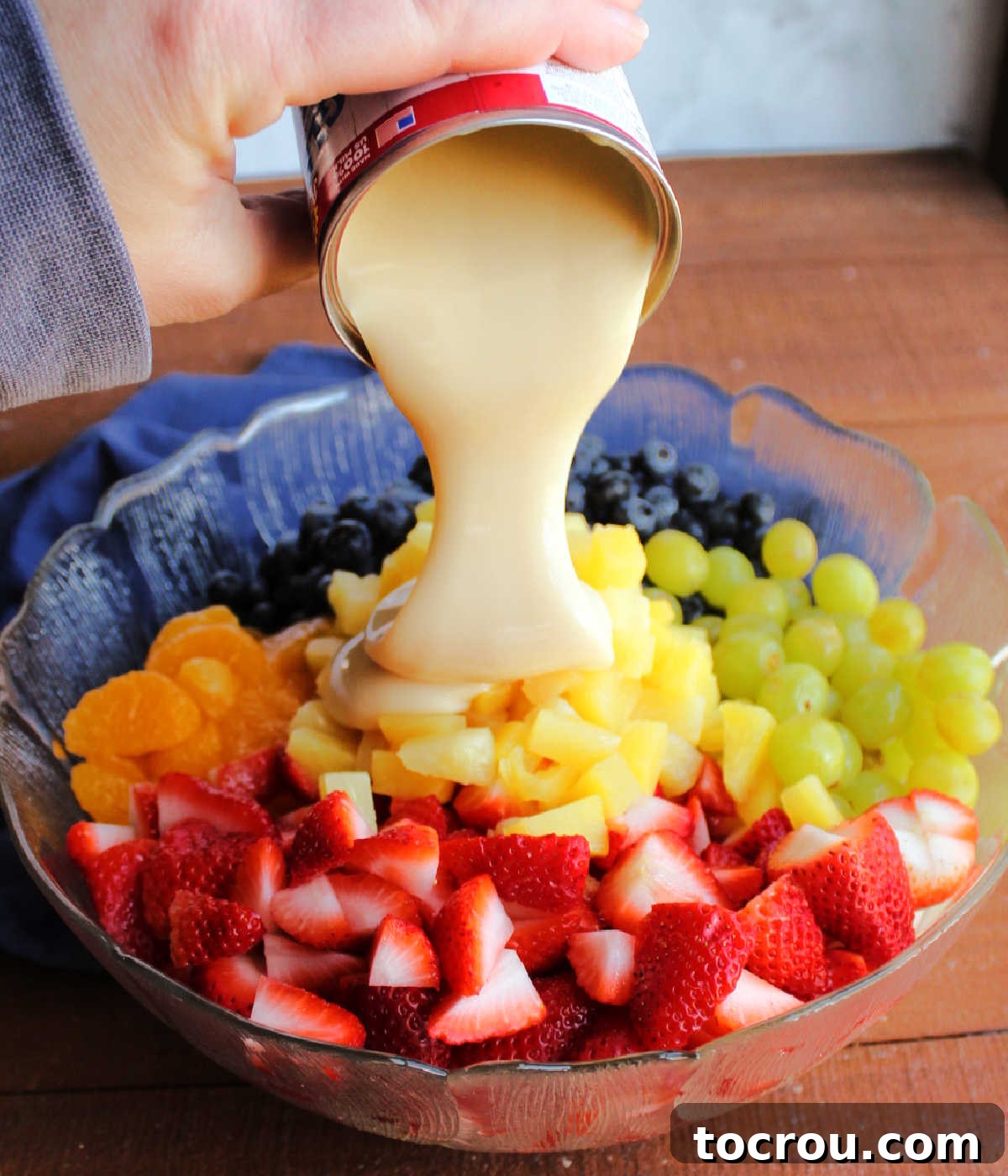 Pouring can of condensed milk over fruit.