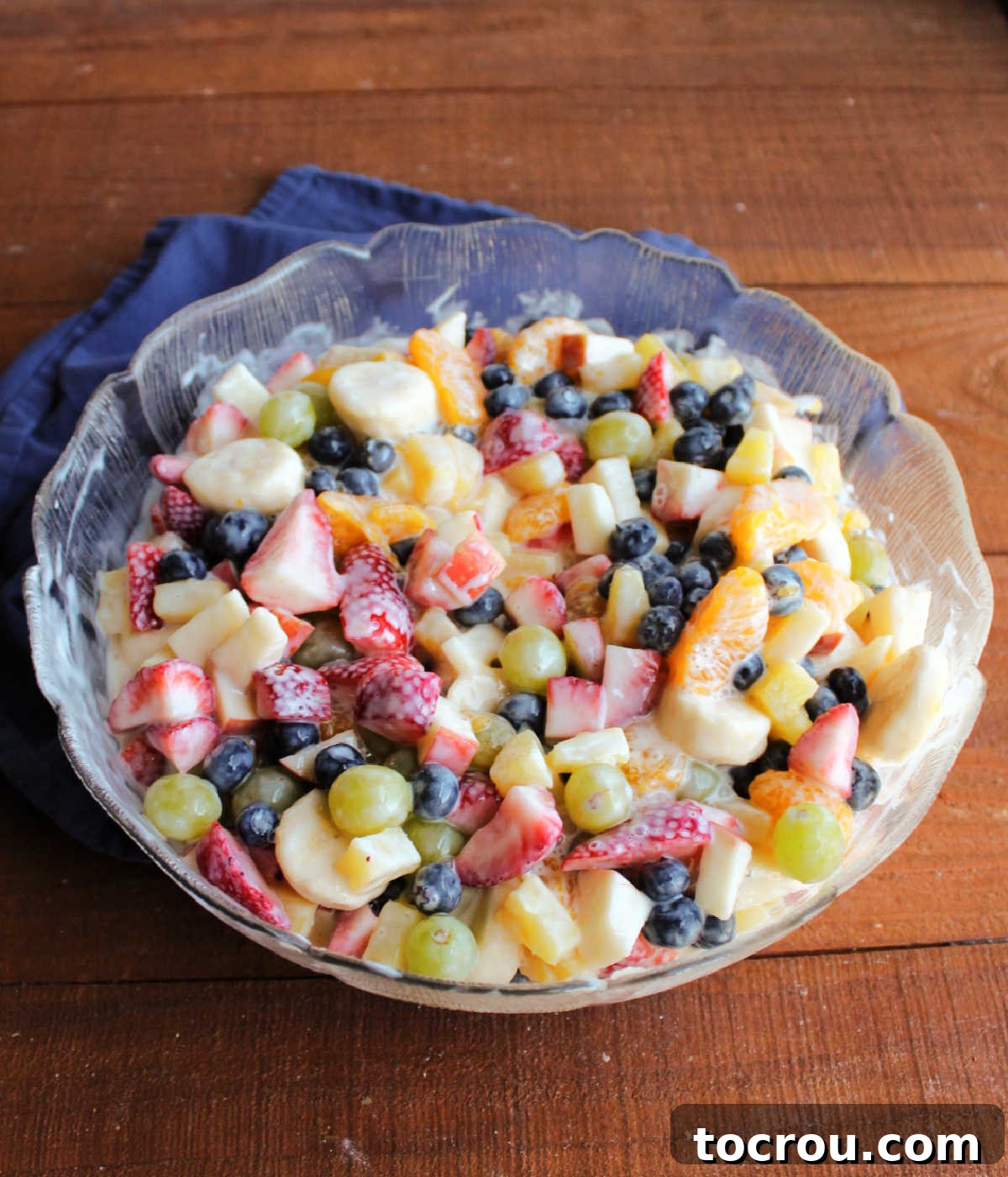 Glass serving bowl of fruit tossed in condensed milk dressing.