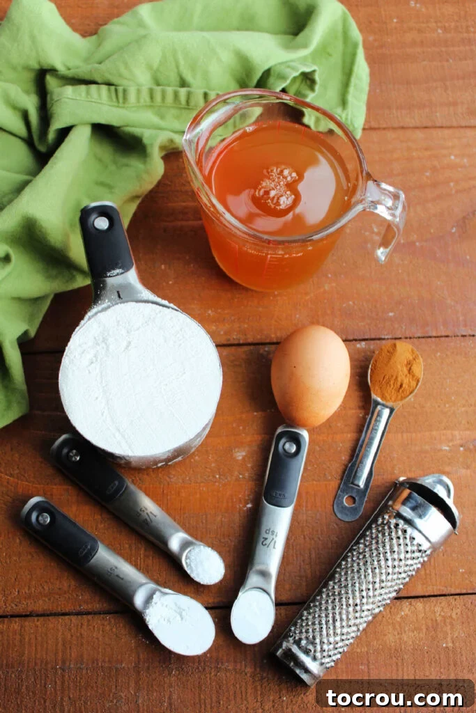 A collection of fresh ingredients laid out for making apple cider waffles, including flour, spices, an egg, and a bottle of apple cider.