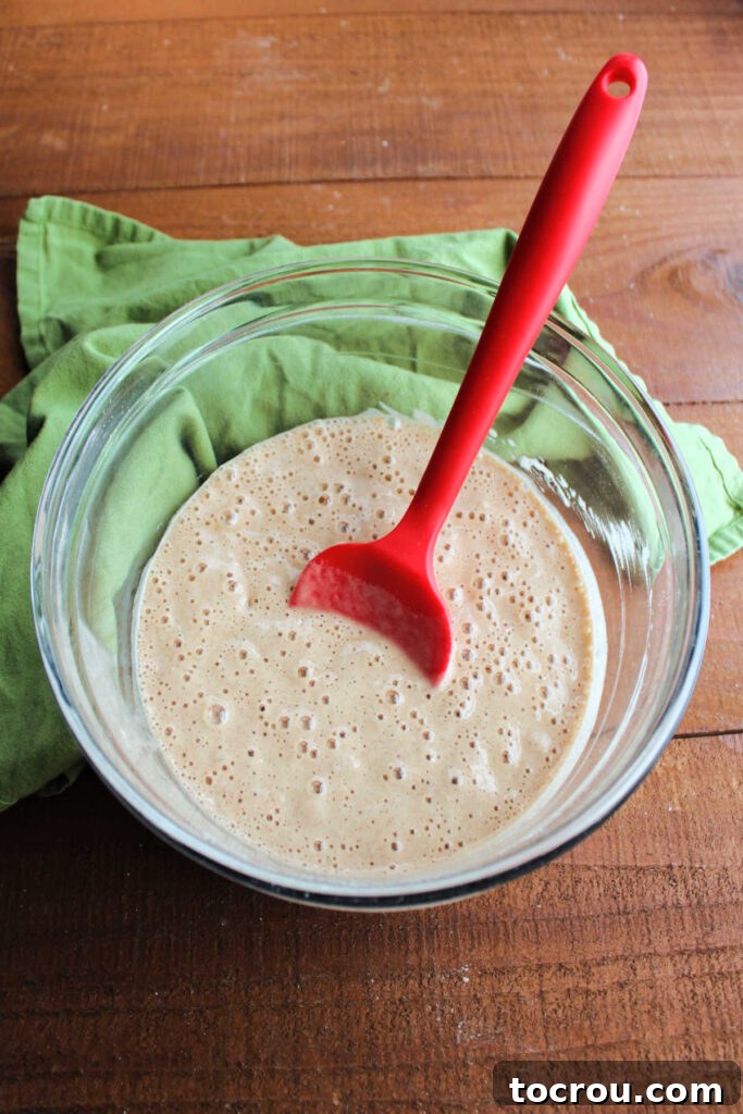 A mixing bowl filled with apple cider waffle batter, showing a smooth yet slightly lumpy consistency, ready for the waffle iron.