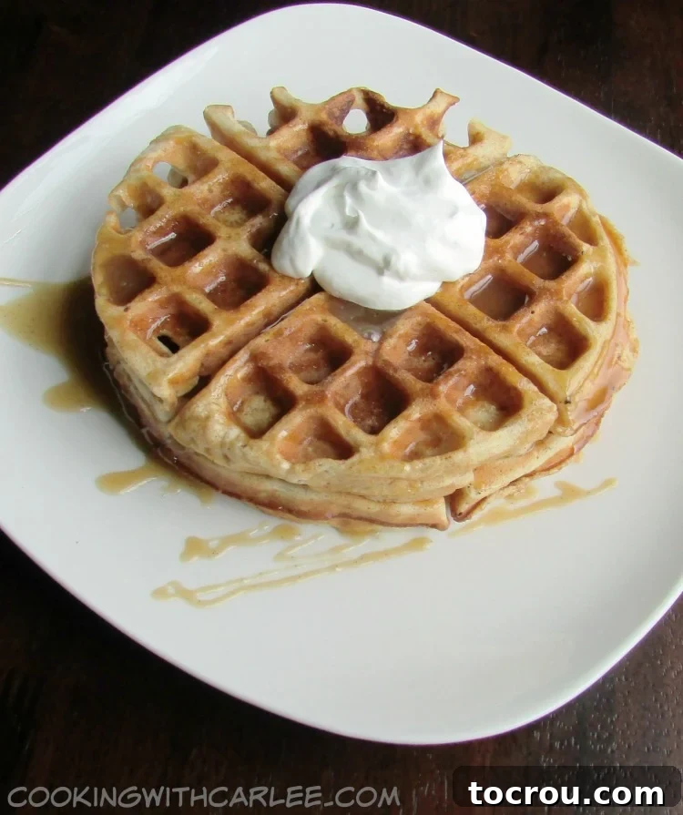 A beautifully presented apple cider waffle, generously topped with creamy whipped cream and a luxurious drizzle of apple cider caramel sauce, ready to be enjoyed.