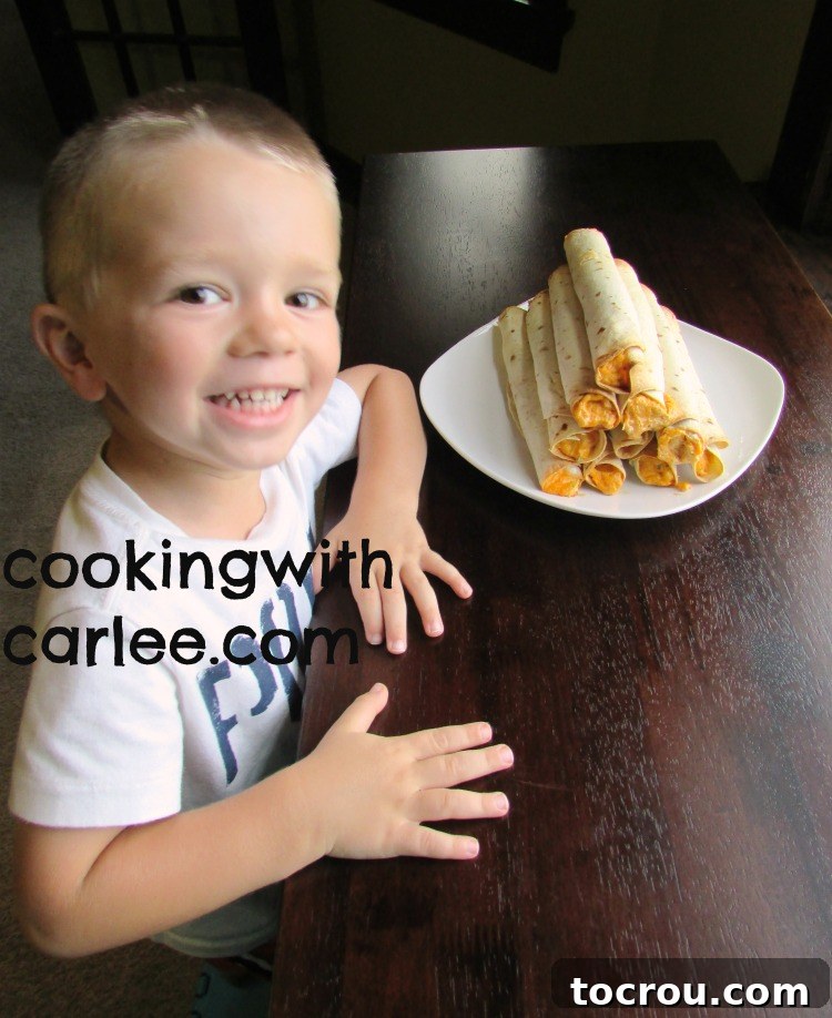 A young boy smiling proudly next to a stack of buffalo chicken taquitos.