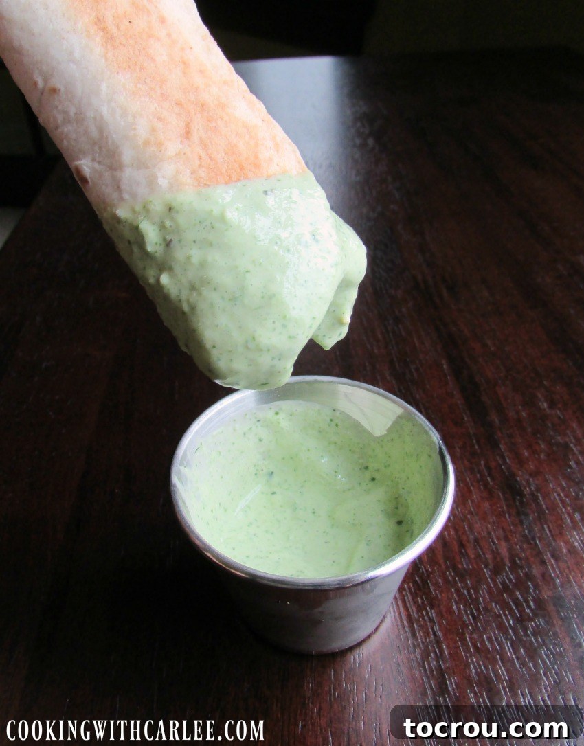 Dipping a crispy buffalo chicken taquito into a bowl of creamy green cilantro sauce.