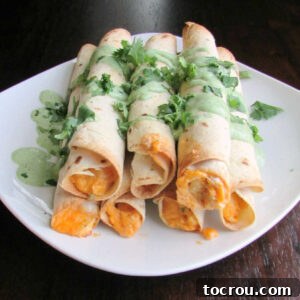 Stack of buffalo chicken taquitos with cilantro cream and chopped cilantro on top.