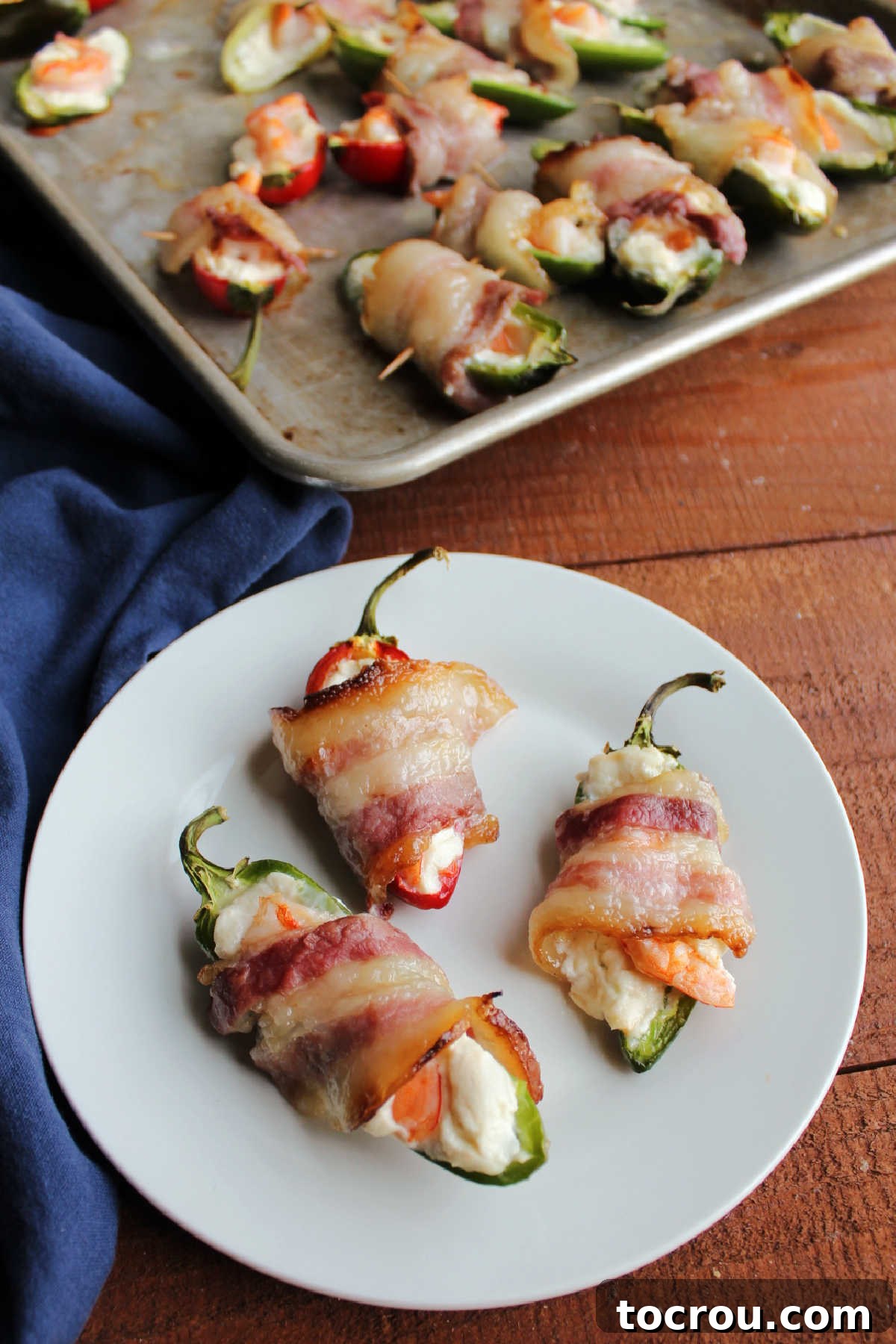 Three shrimp stuffed jalapenos with cream cheese and bacon on small plate ready to eat. 