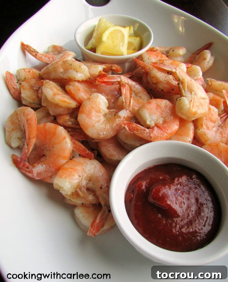 A generously filled platter of roasted shrimp, ready to be enjoyed, served alongside a small ramekin of fresh lemon wedges and another of classic cocktail sauce for dipping.