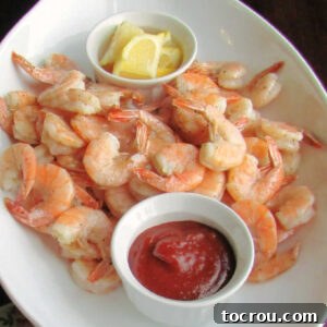 Platter of lemon roasted shrimp with bowl of cocktail sauce and bowl of lemon wedges.