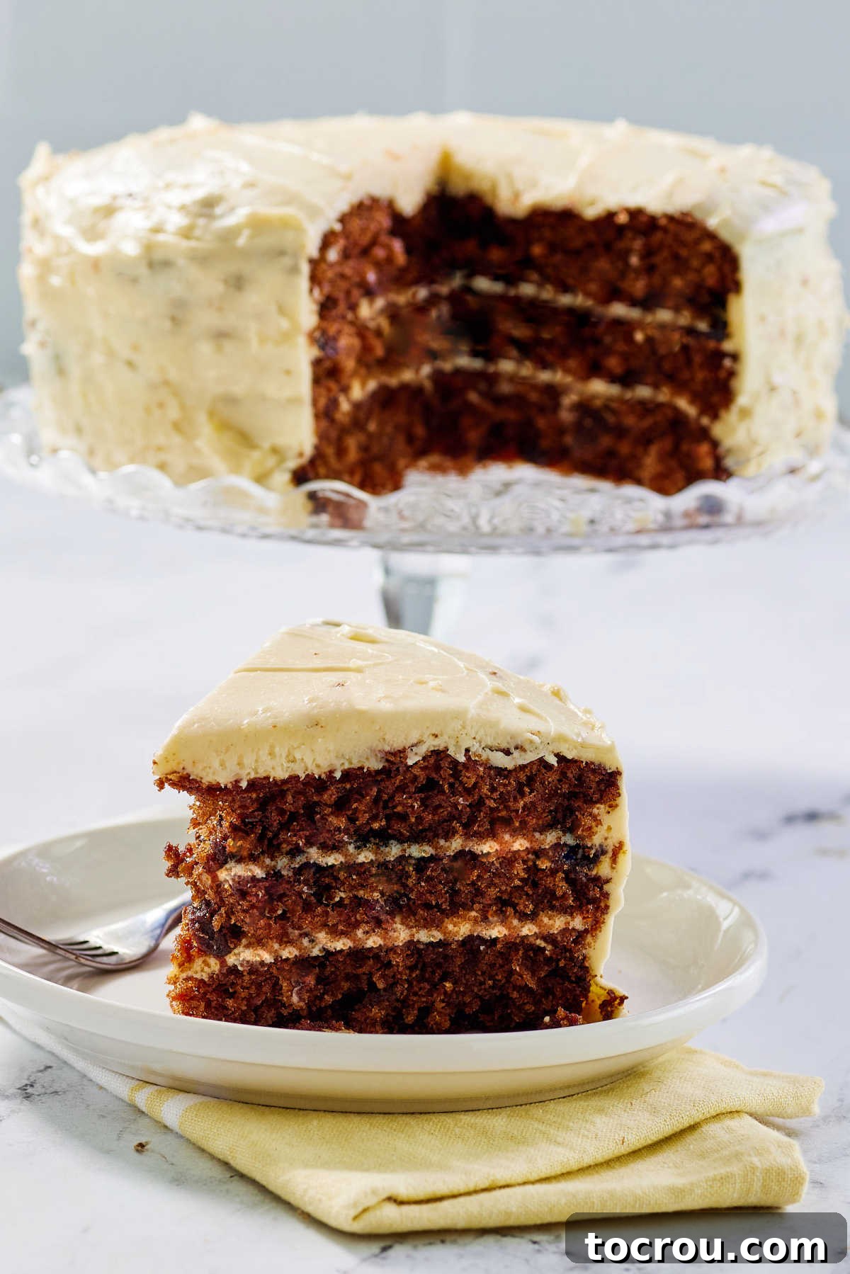 Wedge of layered carrot cake with cream cheese frosting showing deep orange color from the carrots and a bit of cocoa powder.
