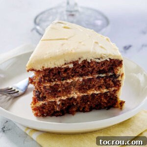Slice of carrot cake with three layers of cake dotted with raisins and cream cheese between the layers and on top of the cake.
