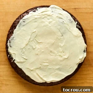 Layer of cream cheese frosting spread over round carrot cake, ready for the next layer.