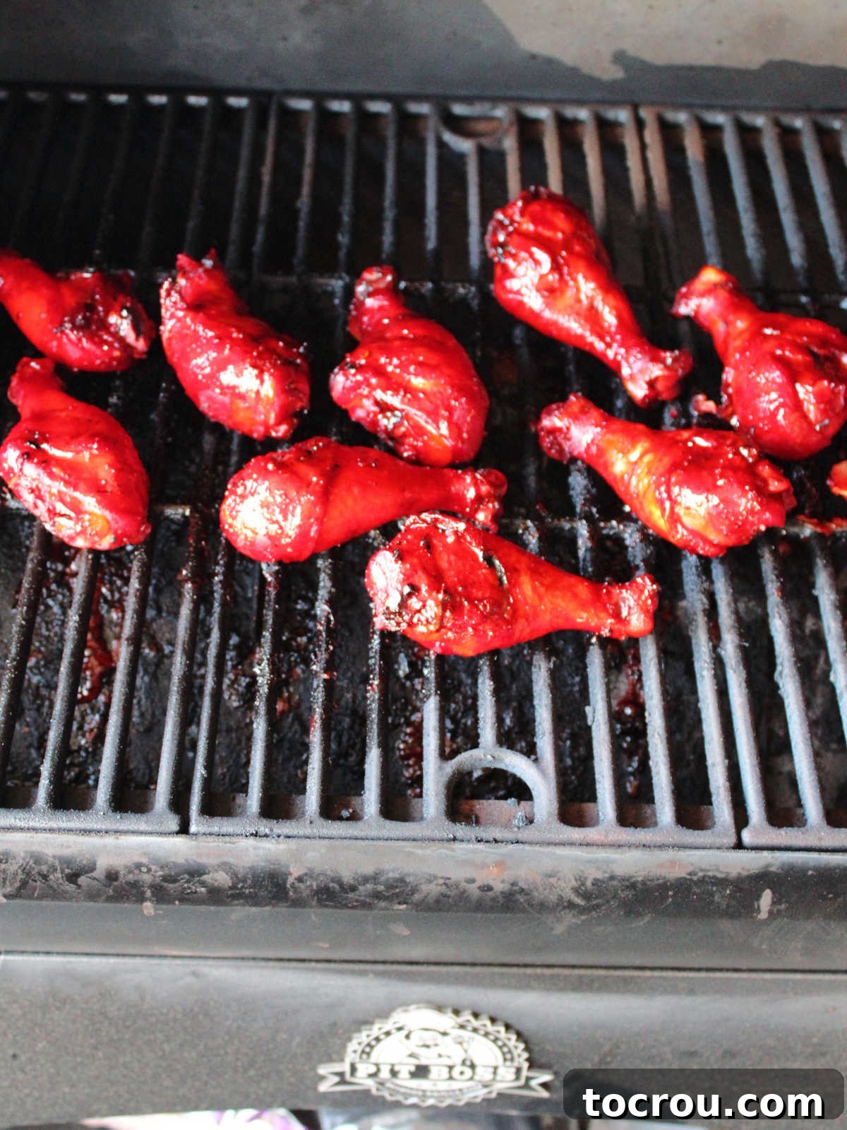 Bright red pieces of char siu chicken cooking on a smoker, developing a beautiful char and glossy finish.