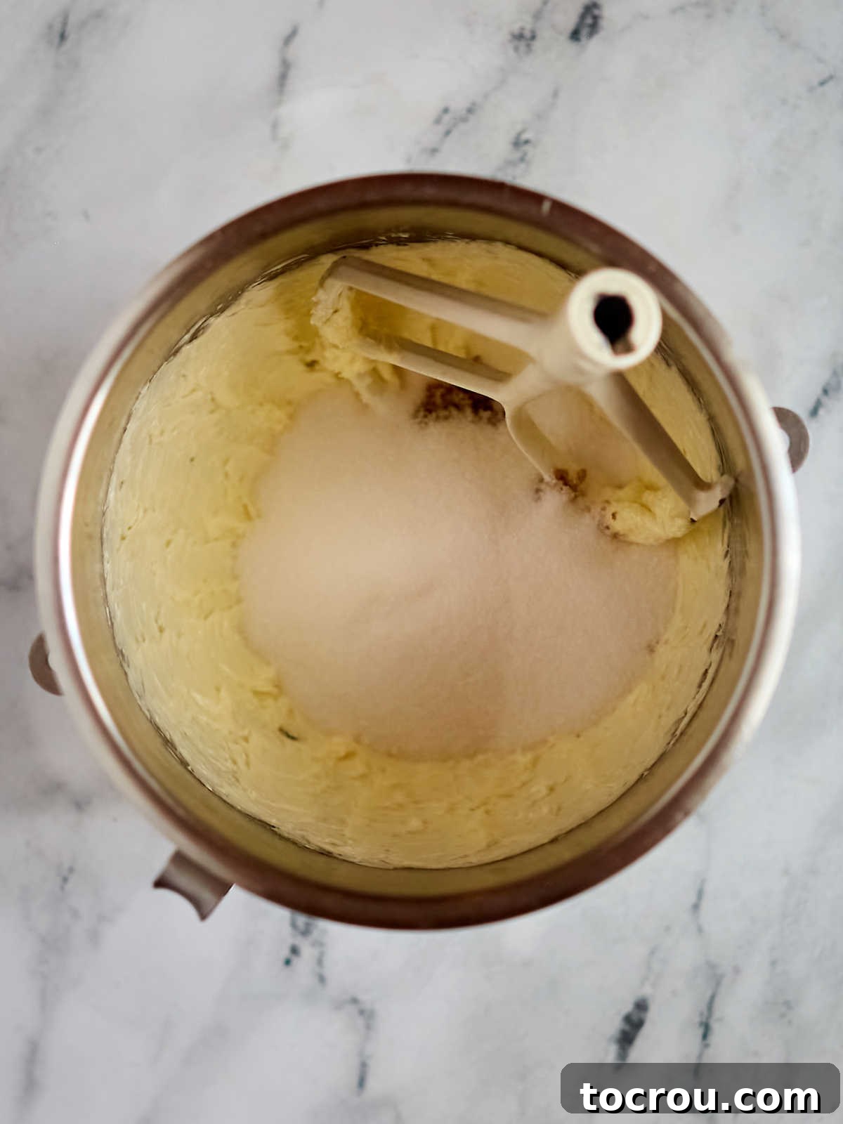 An up-close shot of a mixer bowl containing perfectly creamed butter and sugar, with the mixer paddle resting inside, indicating the initial steps of preparing the cake batter for a delicious blueberry layer cake with cream cheese frosting.