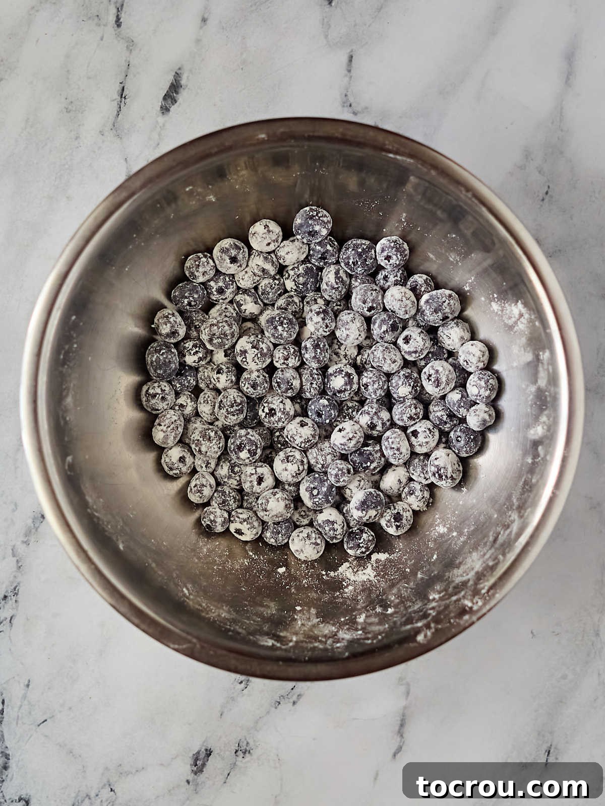 A bowl filled with fresh, vibrant blueberries that have been lightly coated in flour, ready to be gently folded into the prepared cake batter. This crucial step ensures the berries are evenly distributed and do not sink during baking, promising a perfect blueberry distribution in every slice.