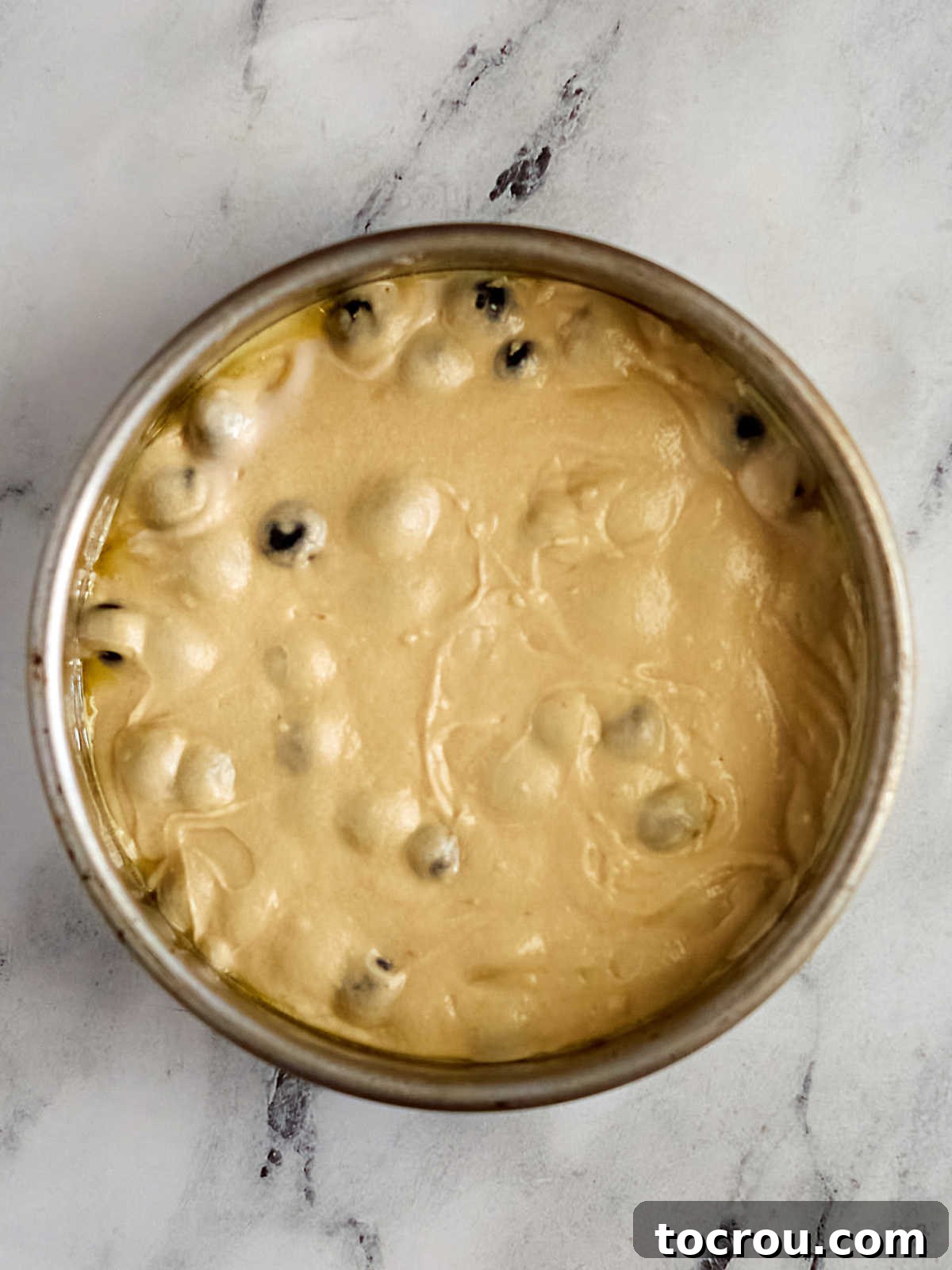 A baking pan filled with a rich, thick lemon blueberry cake batter, smooth and ready to be placed into the oven for baking. The batter is speckled with blueberries, promising a moist and flavorful cake upon completion.