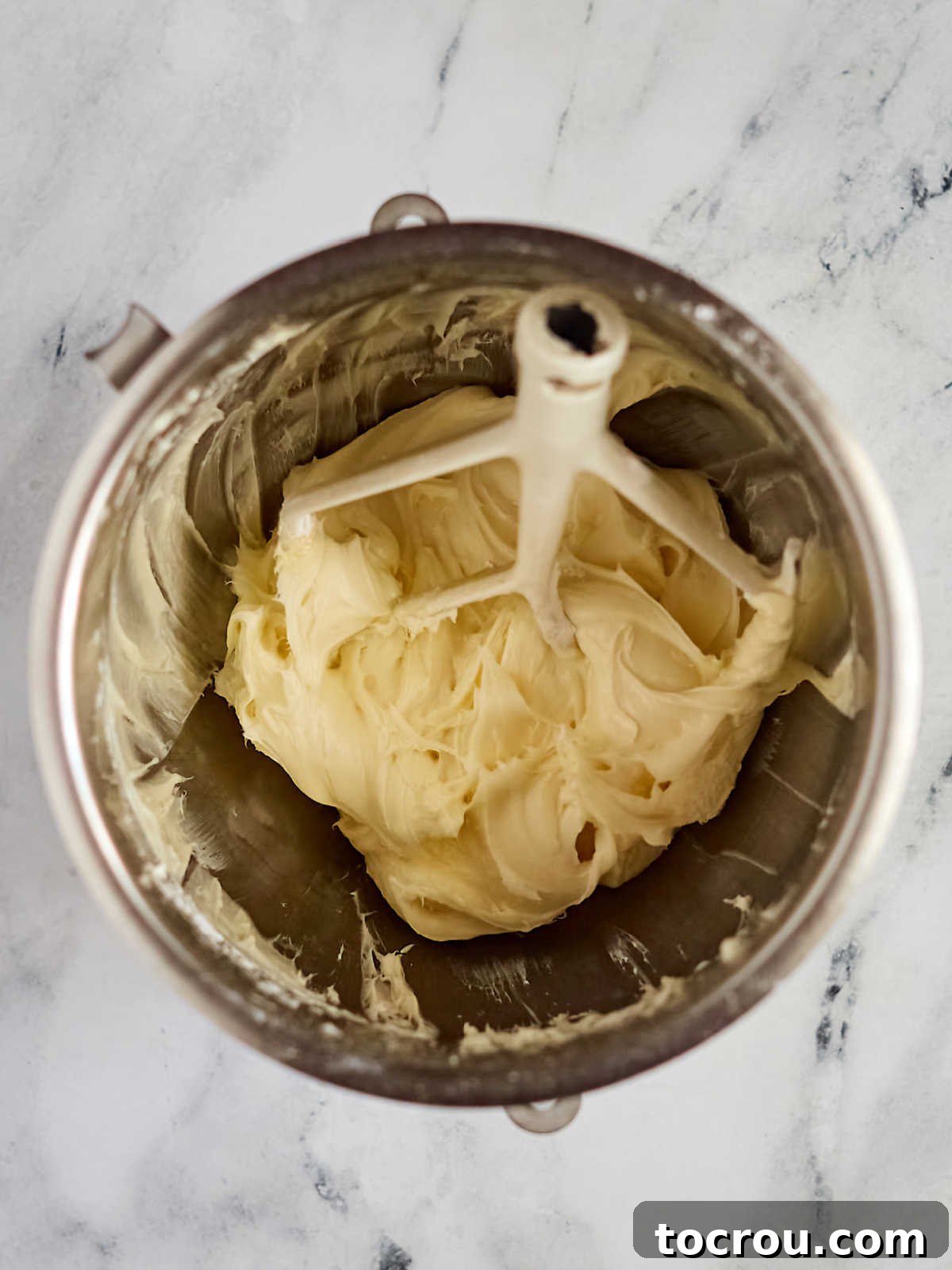 A stainless steel mixer bowl filled with freshly made, smooth, and creamy homemade cream cheese frosting, perfectly whipped and ready to be spread generously between the cake layers and on top of a delicious lemon blueberry cake, promising a rich and decadent finish.